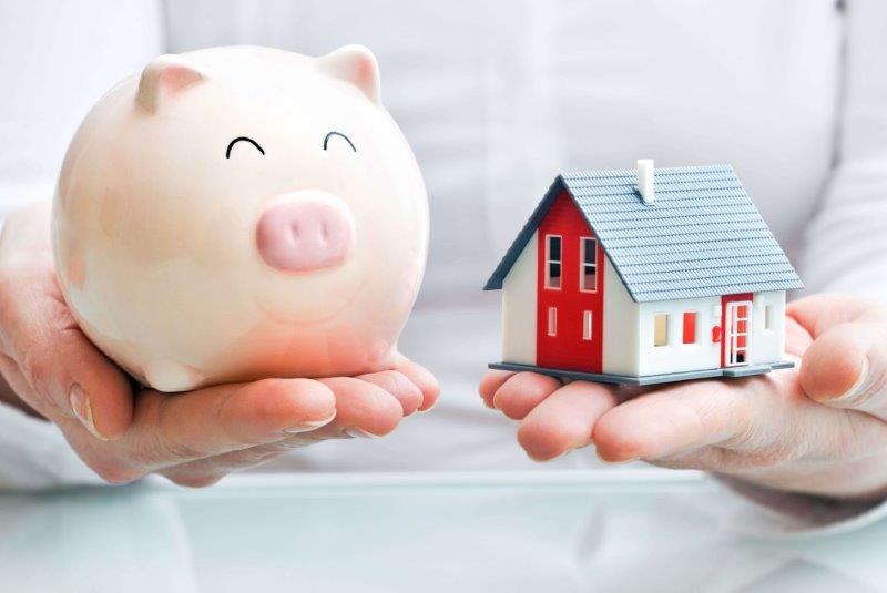 A person holding a puggy bank in one hand and a toy house in another