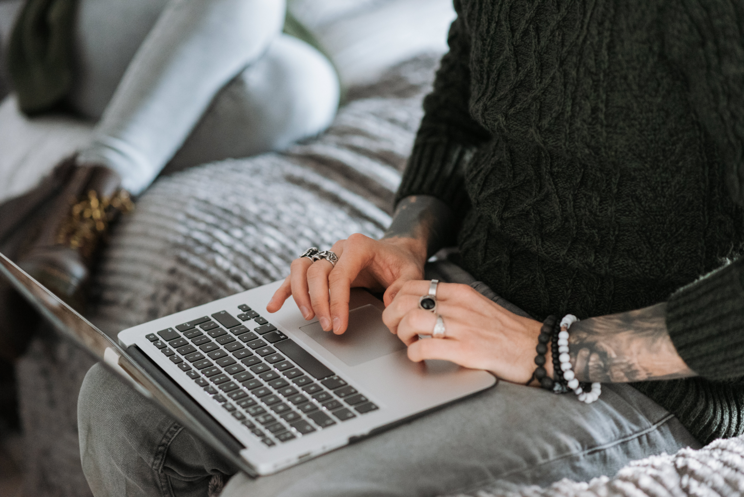 Woman with tattoos and jewellery typing on laptop